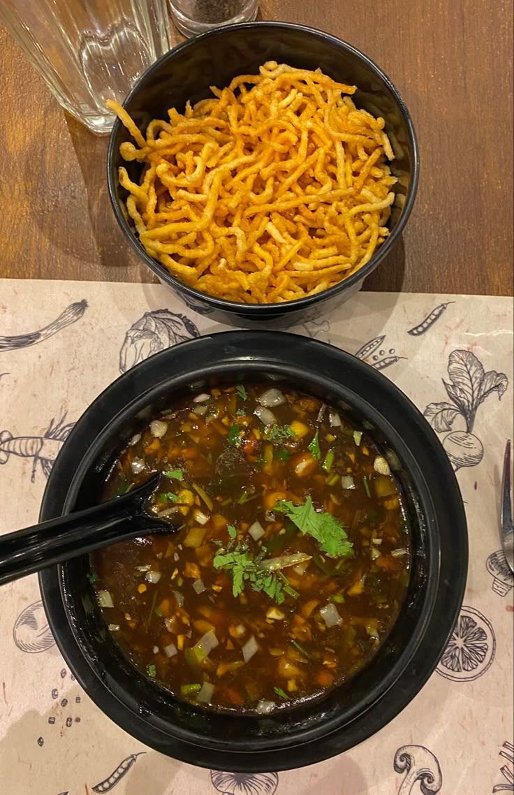 Indo-Chinese Manchow soup in a black bowl served with a side of crispy fried noodles.