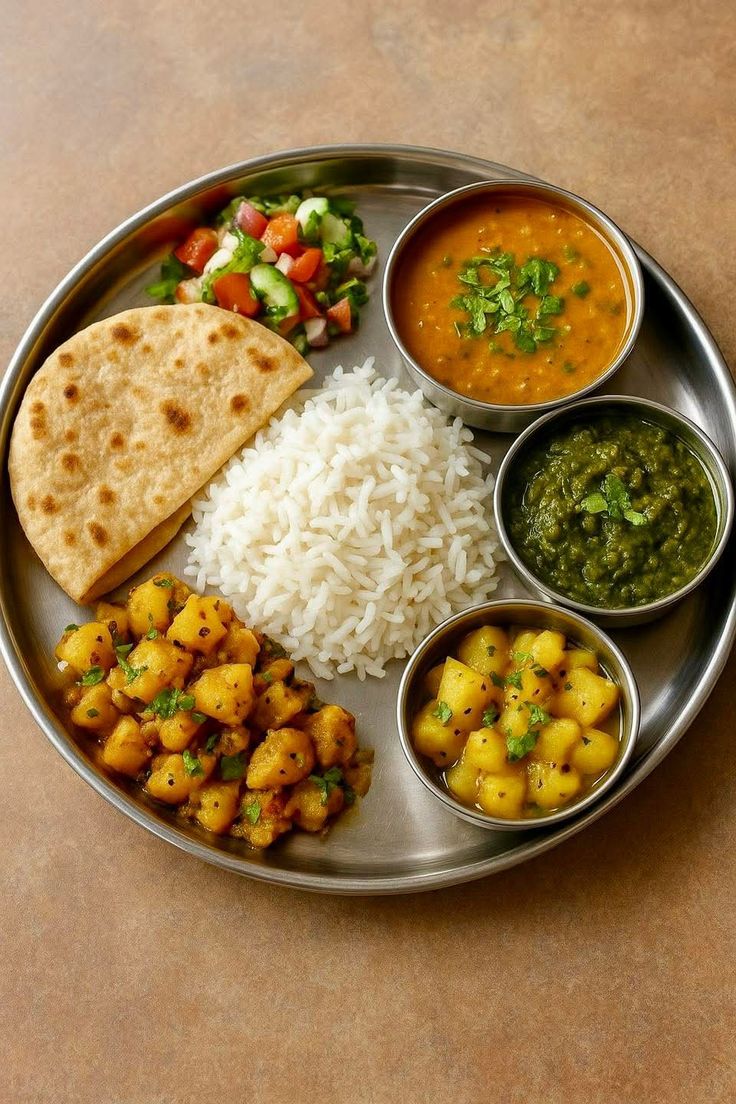 Traditional Indian veg thali platter with dal, saag, aloo sabzi, steamed rice, and roti.