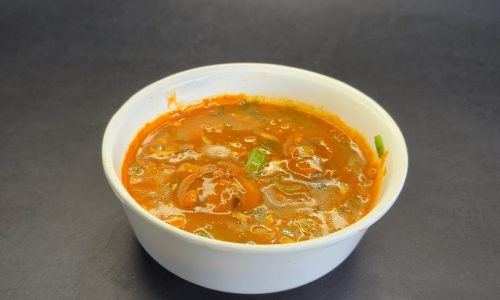 An angled shot of a classic Indo-Chinese Manchurian soup or gravy dish in a simple white bowl.