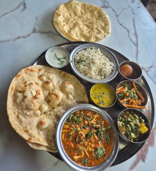 A complete Indian deluxe thali platter with assorted savory dishes, fresh flatbread, and a dessert.