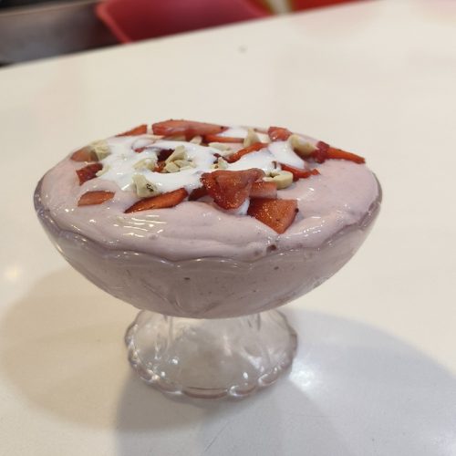 Creamy strawberry cream dessert served in a glass goblet bowl, topped with sliced fresh strawberries and nuts.