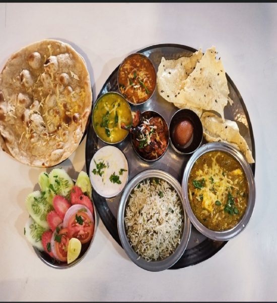 Deluxe Indian thali served with bowls of mixed curries, raita, crispy papadum, flatbread, and a fresh side salad.